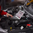 Automotive technician using laptop for engine diagnostics in vehicle engine bay