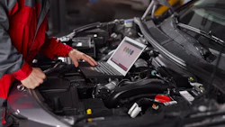 Automotive technician using laptop for engine diagnostics in vehicle engine bay