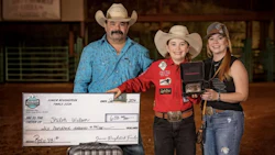Three rodeo competitors posing with award check and trophy in indoor arena
