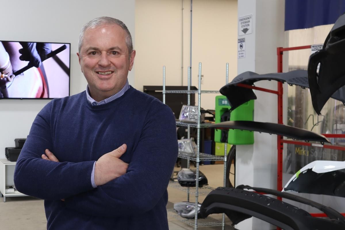 Smiling professional in blue sweater standing in technical workshop with automotive equipment