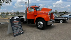 Vintage orange Mack truck on display in parking lot with informational sign