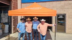 Simplicity branded orange tent with four cowboys standing outside an office building