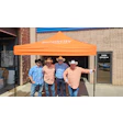 Simplicity branded orange tent with four cowboys standing outside an office building