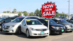 White and black cars for sale at a dealership with a red 'Now on Sale' sign