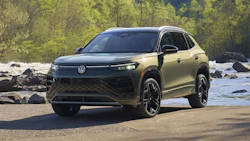Olive green Volkswagen SUV parked by rocky river with forest background