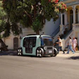 Autonomous mint green vehicle parked on urban street with pedestrians nearby