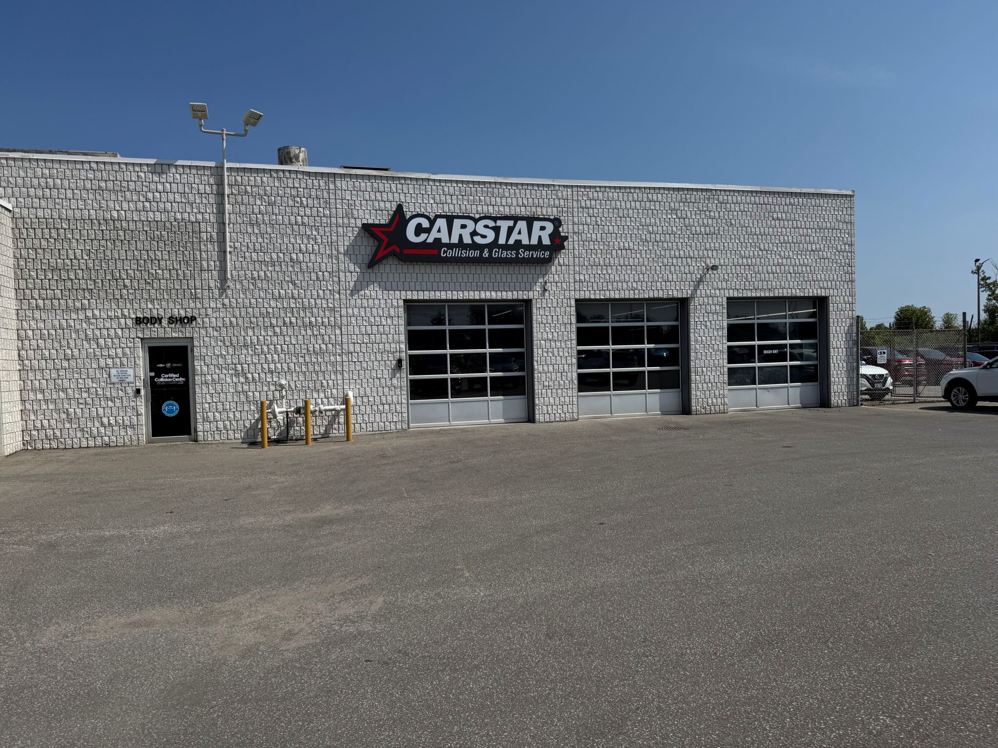 CARSTAR auto collision repair shop with white brick exterior and three garage doors