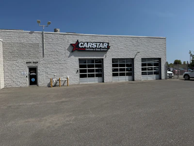 CARSTAR auto collision repair shop with white brick exterior and three garage doors