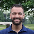 Smiling man in blue polo shirt standing outdoors with trees in background