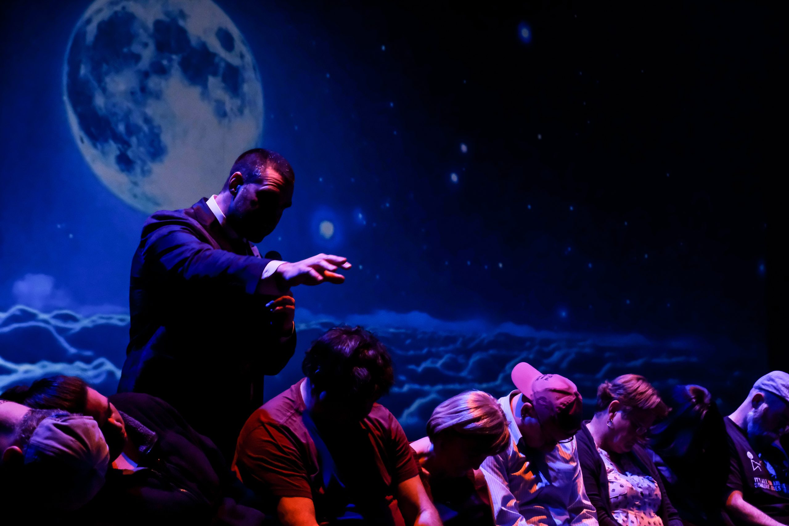 Presenter gesturing on stage with starry night and full moon backdrop