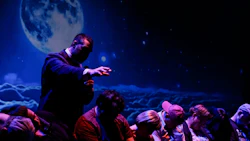 Presenter gesturing on stage with starry night and full moon backdrop