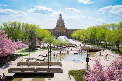 Alberta Legislature Building with water fountain, pink cherry blossoms, and green trees on a sunny spring day