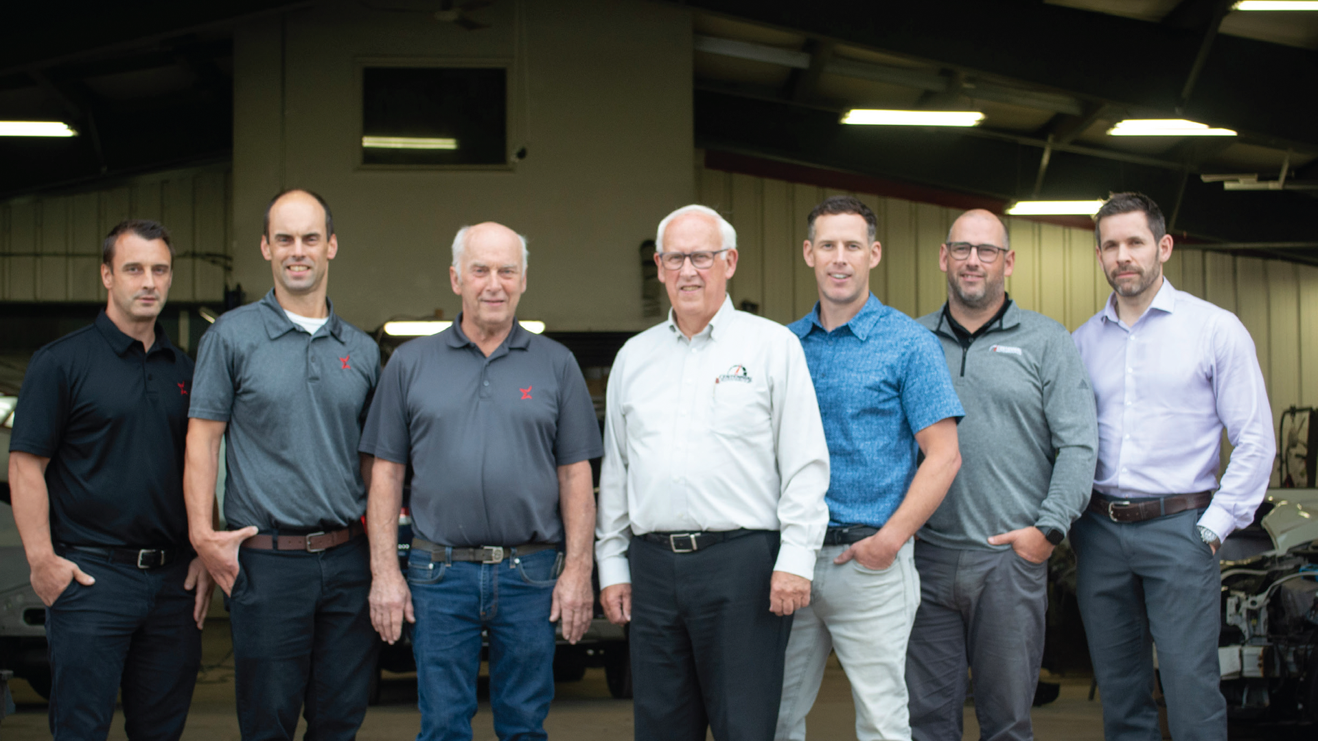 Seven professional men standing in a workplace, wearing business casual attire