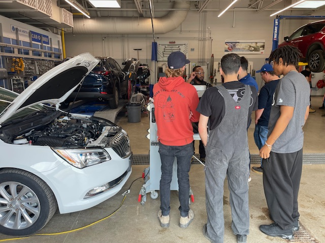 Auto technicians examining a white car with open hood in repair shop