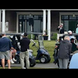 Golfers gathered with golf carts at outdoor event near brick building