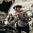 Automotive technicians in camouflage jacket examining car engine in repair shop