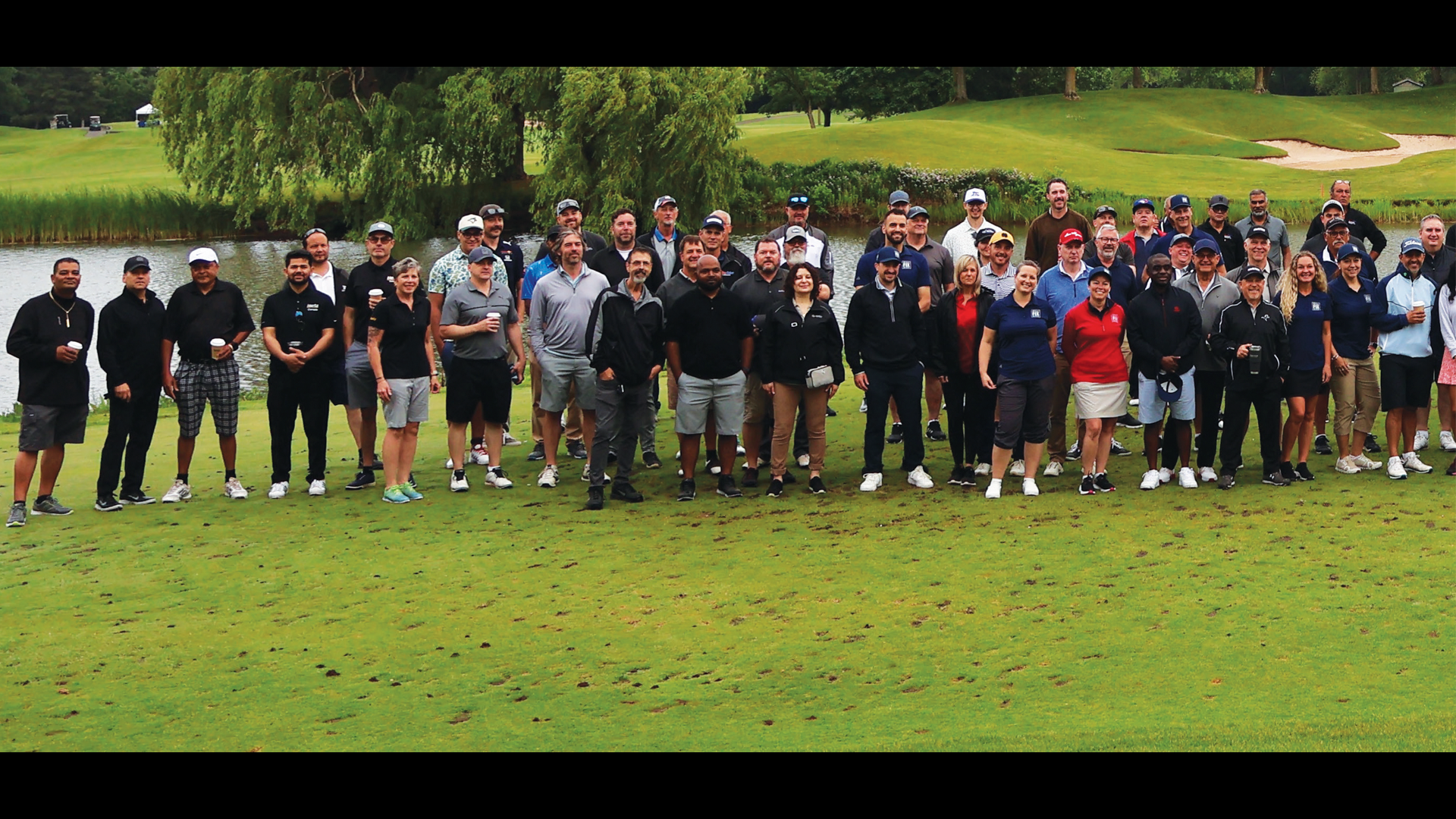Large group of golfers posing together on a green golf course near a water hazard