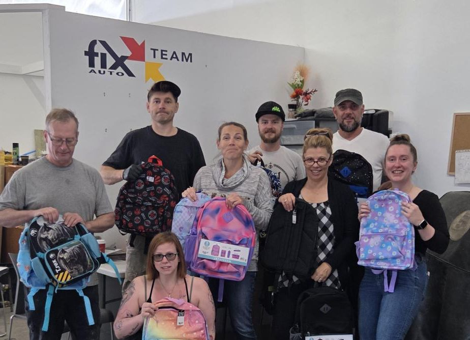 Fix Auto Team group photo with employees holding colorful backpacks