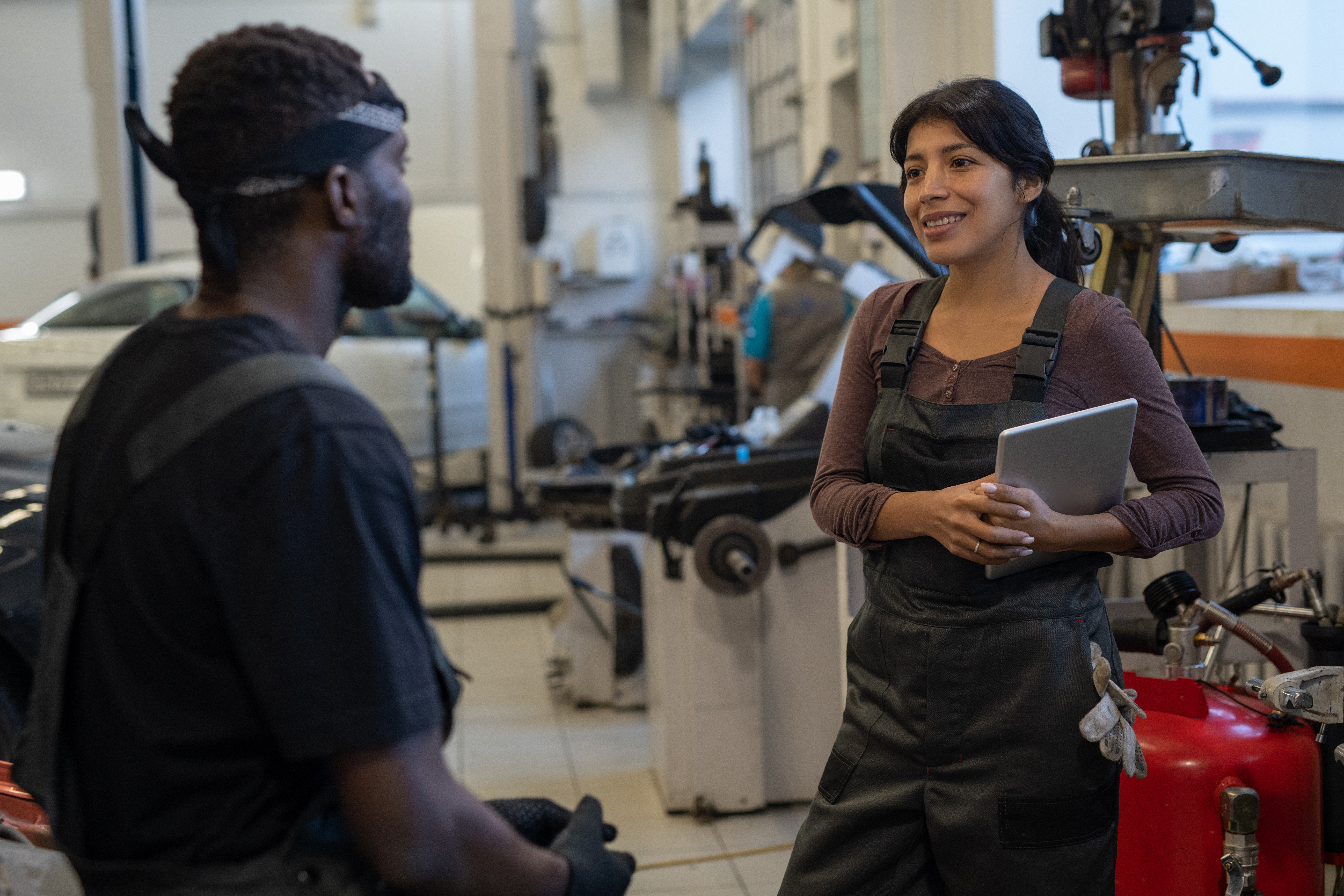 Two workers in an industrial workshop, discussing project with machinery in background