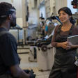 Two workers in an industrial workshop, discussing project with machinery in background