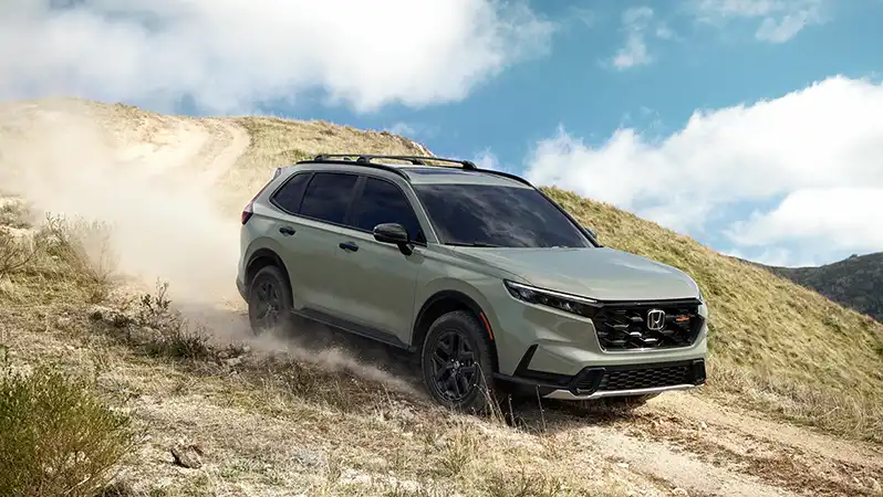 Green Honda SUV driving on dusty mountain terrain with cloudy sky