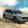 Green Honda SUV driving on dusty mountain terrain with cloudy sky