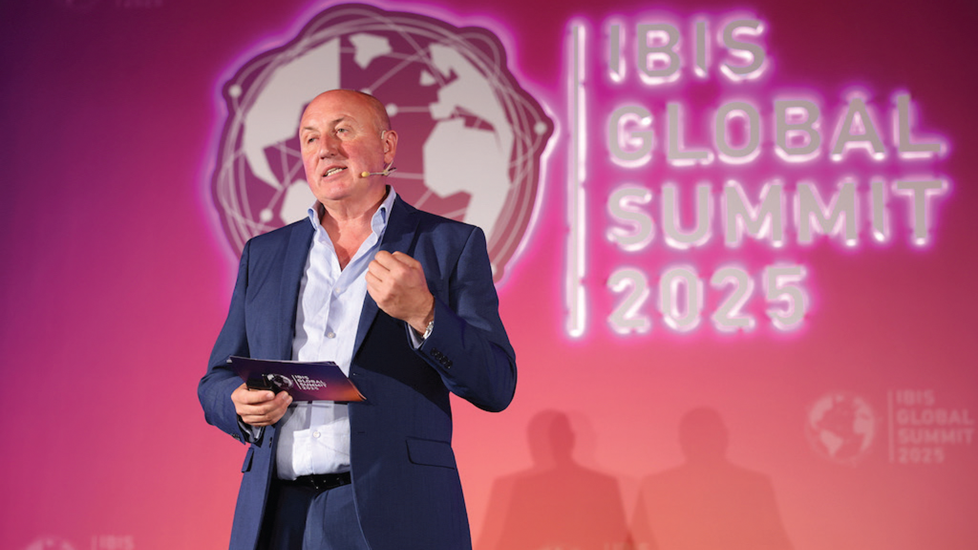 Professional speaker presenting at IBIS Global Summit 2025 on pink background