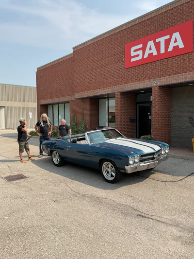 SATA logo on brick building with classic blue convertible parked outside