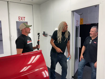 Three men standing near red equipment and exit sign in industrial setting