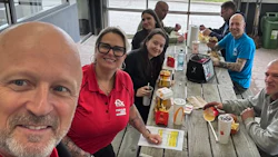 Group of colleagues enjoying lunch at a wooden table with food and drinks