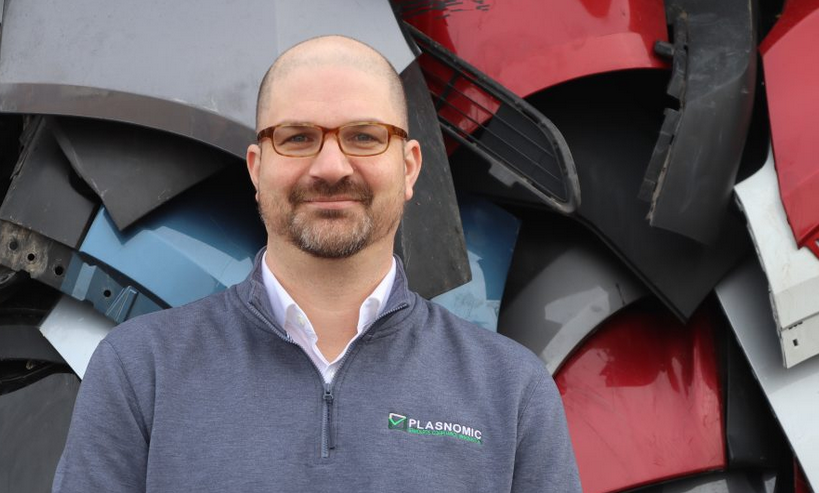 Professional wearing glasses in gray zip-up shirt standing near industrial machinery