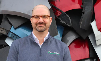 Professional wearing glasses in gray zip-up shirt standing near industrial machinery