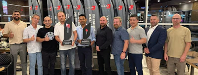 Group of nine professionals posing together at corporate event with branded backdrop