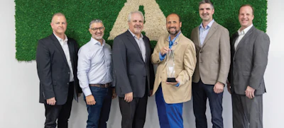 Six businessmen in professional attire posing together against a green hedge backdrop