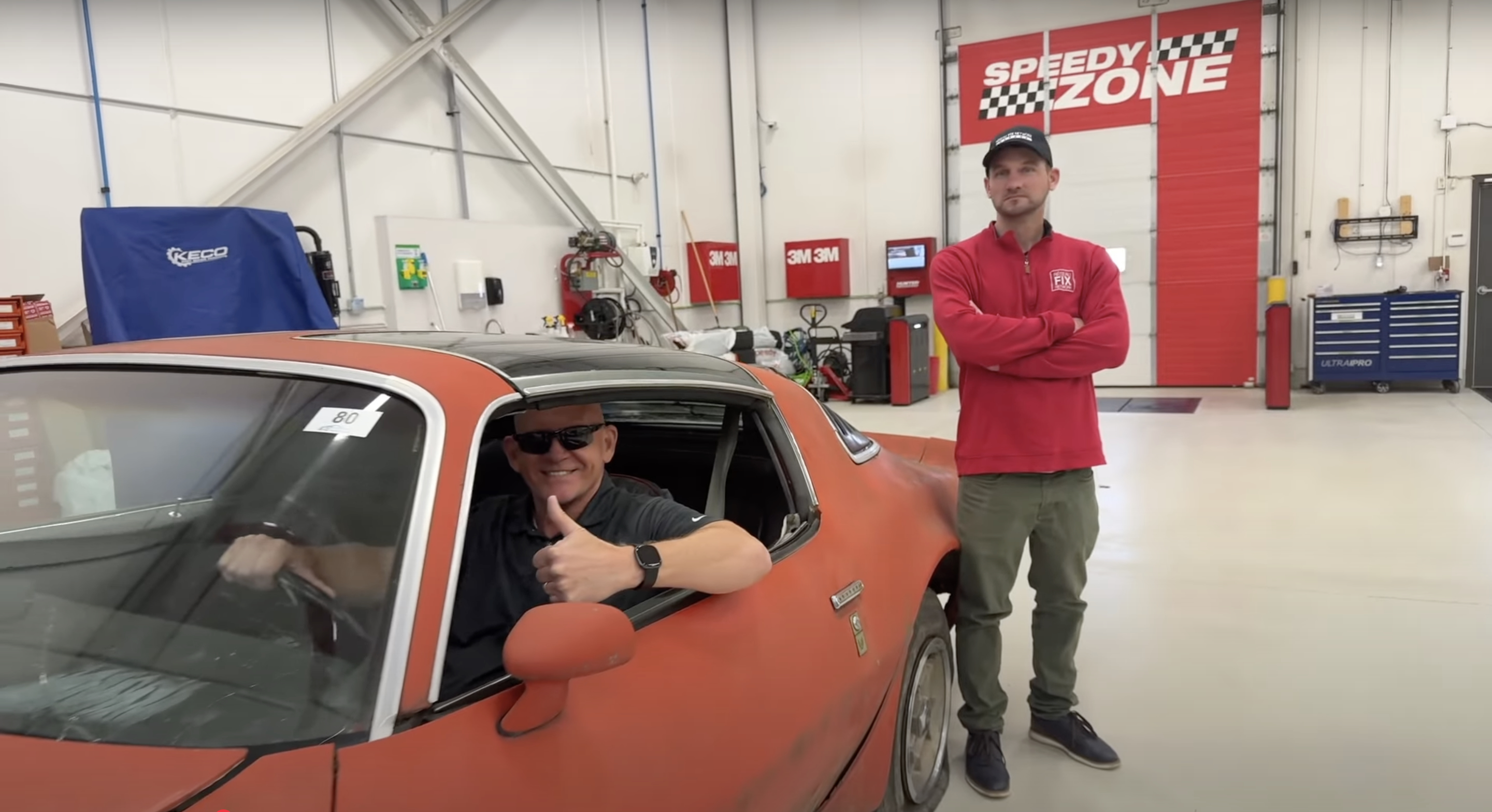 Classic orange muscle car in auto repair shop with technician standing nearby