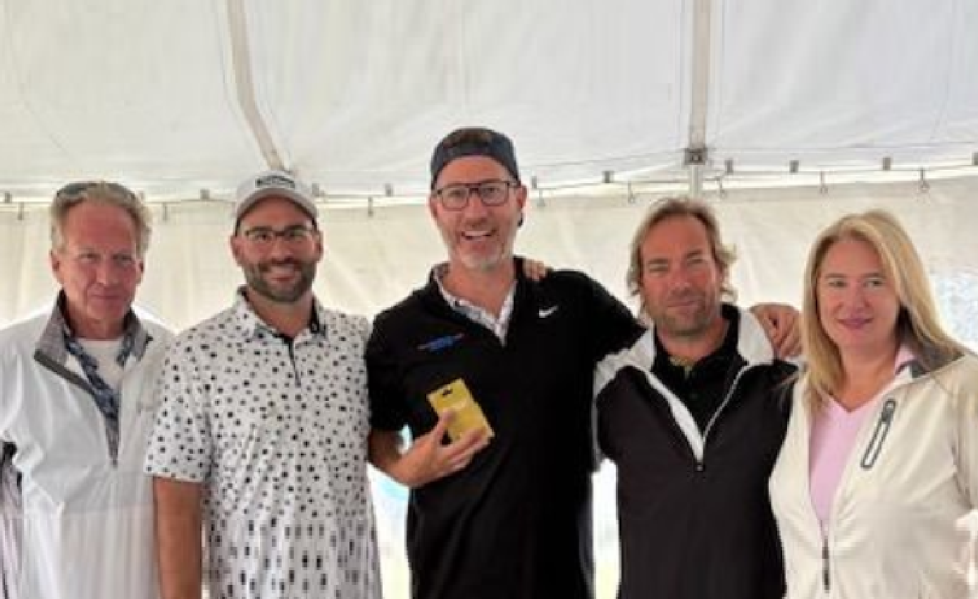 Five professionals posing together in a white event tent, wearing casual business attire