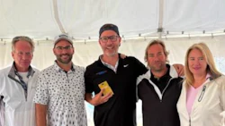 Five professionals posing together in a white event tent, wearing casual business attire