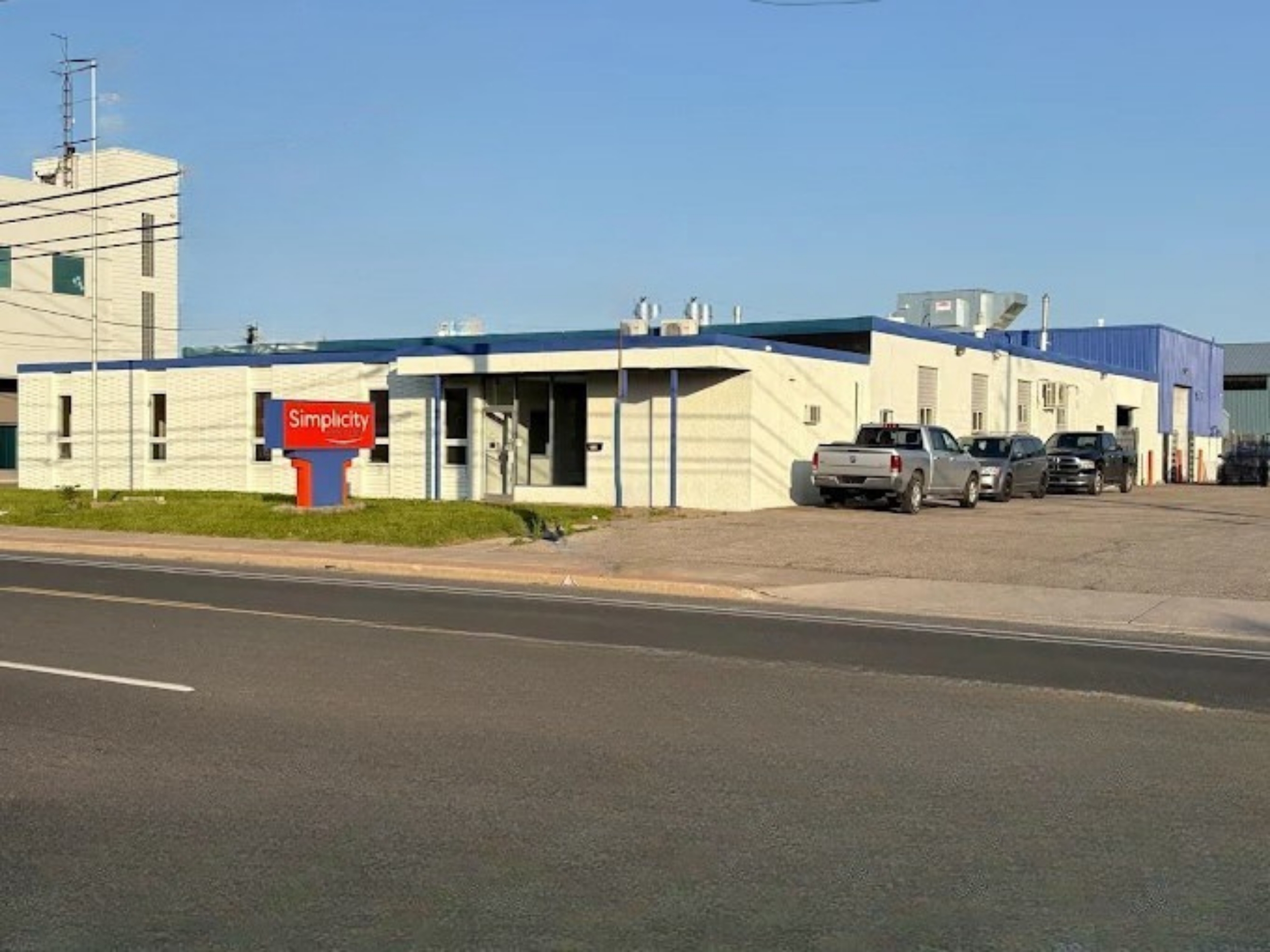 Simplicity business building with red logo sign, parked trucks, and clear blue sky
