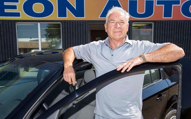 Senior car salesman standing beside a black vehicle at Eon Auto dealership