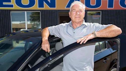 Senior car salesman standing beside a black vehicle at Eon Auto dealership