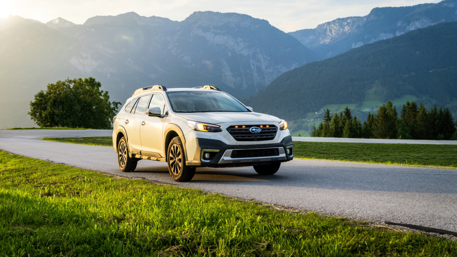 White Subaru SUV driving on mountain road with alpine landscape