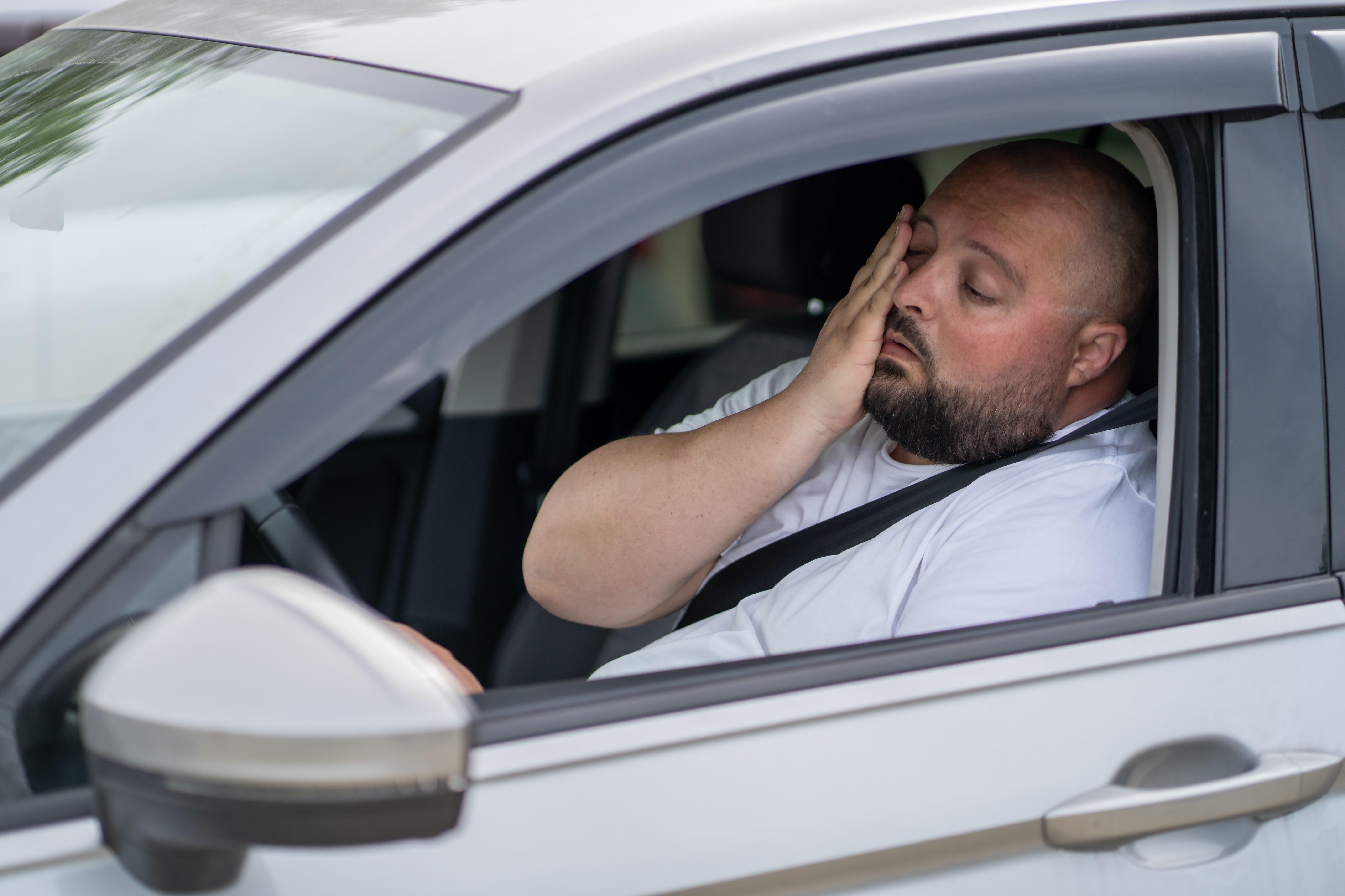 Fatigued driver resting head on hand inside white car