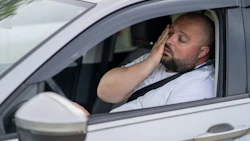 Fatigued driver resting head on hand inside white car