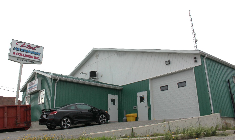 Green auto body shop building with City Collision Inc. sign and black car