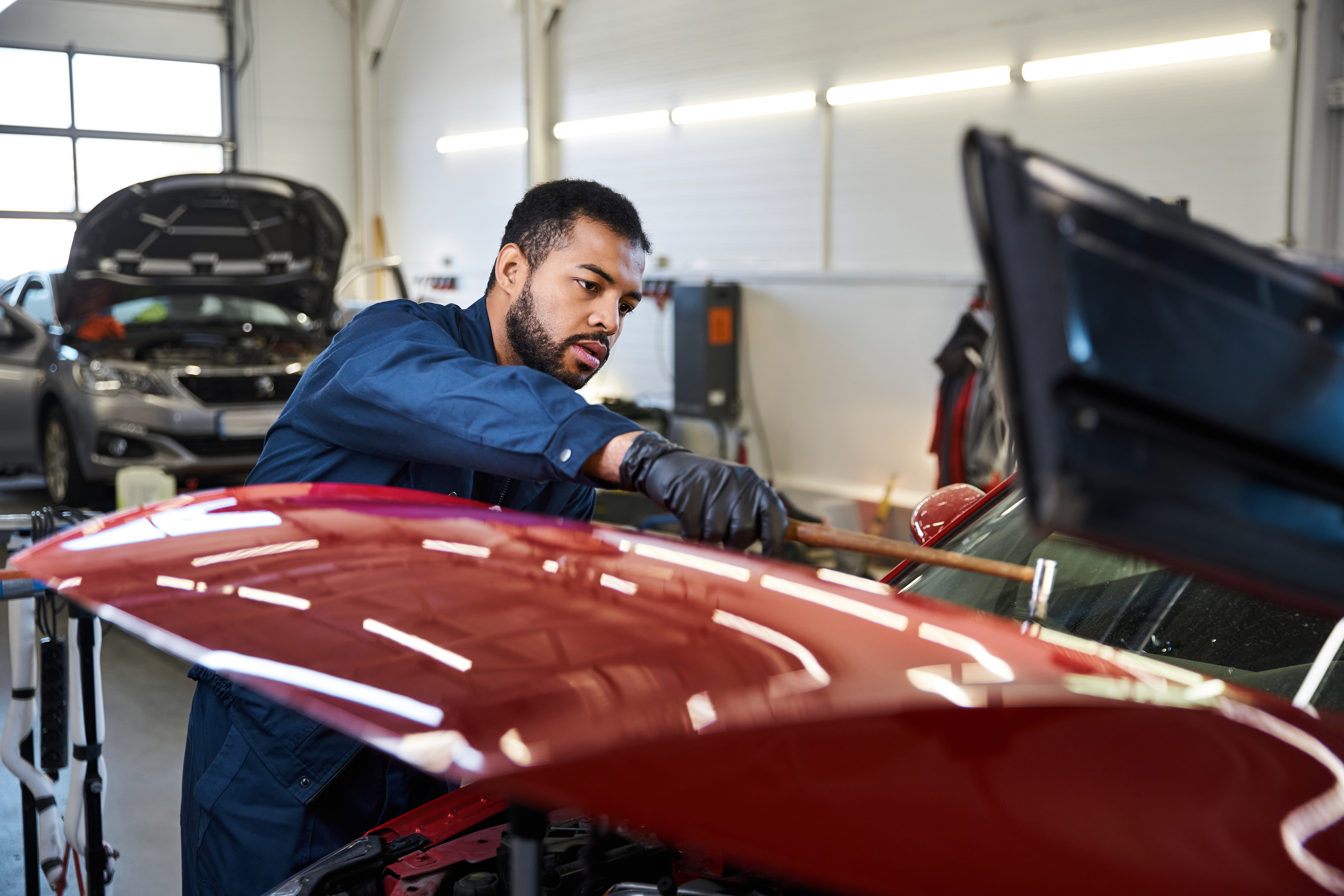 Auto mechanic in blue uniform inspecting a red car in a repair shop