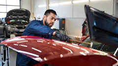 Auto mechanic in blue uniform inspecting a red car in a repair shop
