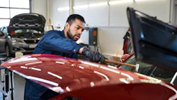 Auto mechanic in blue uniform inspecting a red car in a repair shop