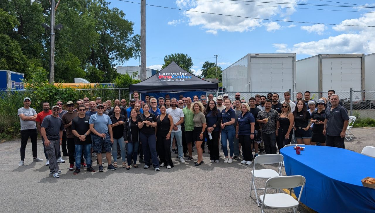 Large group of employees gathered outdoors at company event with blue tent