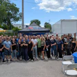 Large group of employees gathered outdoors at company event with blue tent