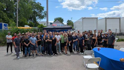 Large group of employees gathered outdoors at company event with blue tent
